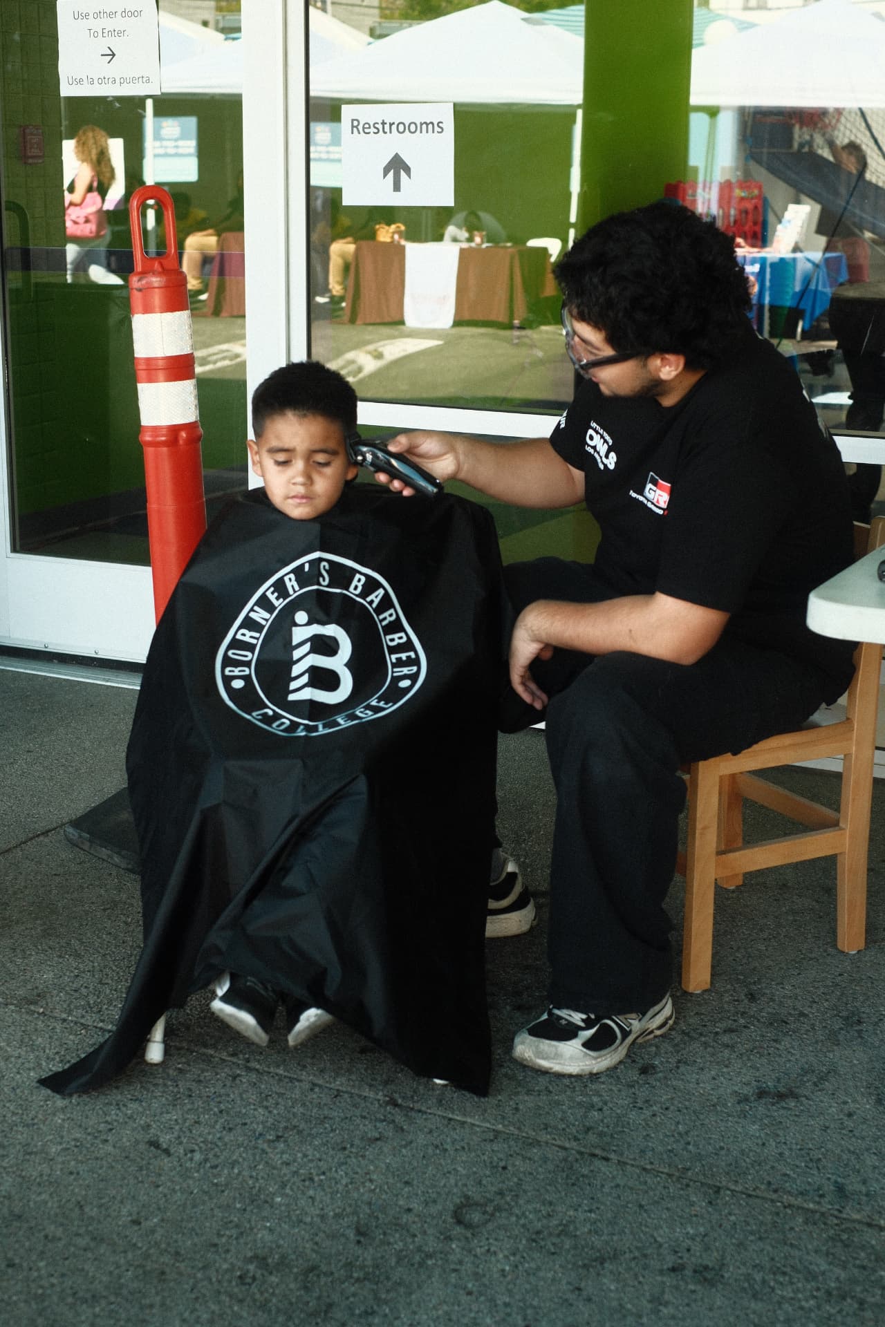 A student barber giving a child a haircut at a community event